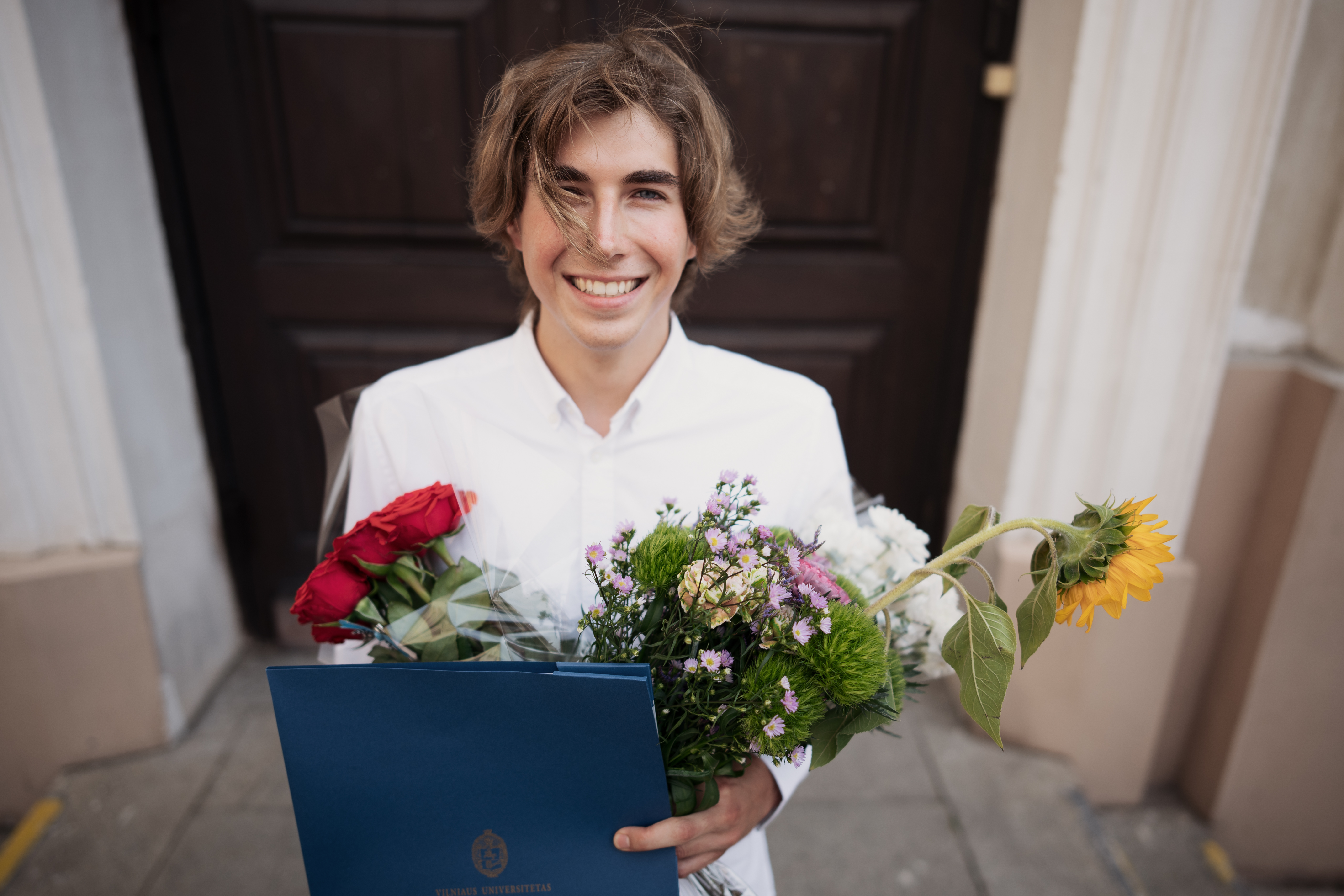 Young graduate holding his diploma in front of a university building.